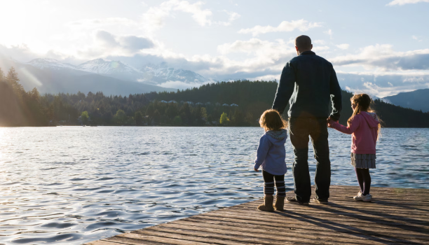 A father and his two children stand on a dock holding hands. 