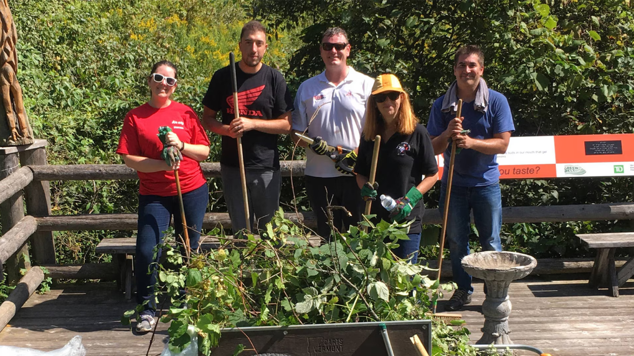 A group of Honda employees doing charitable work pose with shovels in a community garden.