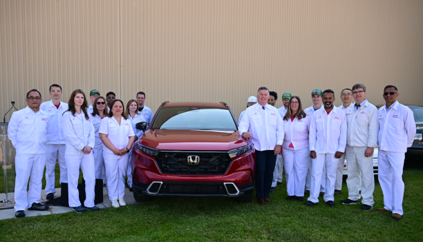 Un groupe d’employés de Honda posant et souriant se tient à côté d’un véhicule Honda rouge.