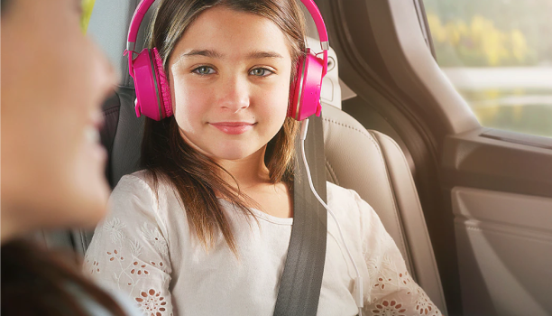 A child wears headphones and smiles from the backseat of a Honda SUV.