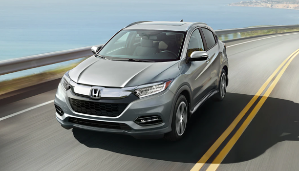 Front view of a Honda SUV is driving on a highway beside a body of water. 